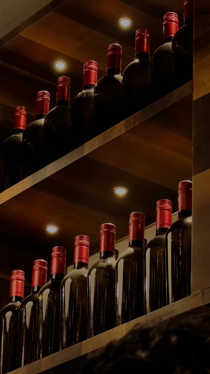 A striking display of wine bottles with red caps on wooden shelves, illuminated by warm lighting.